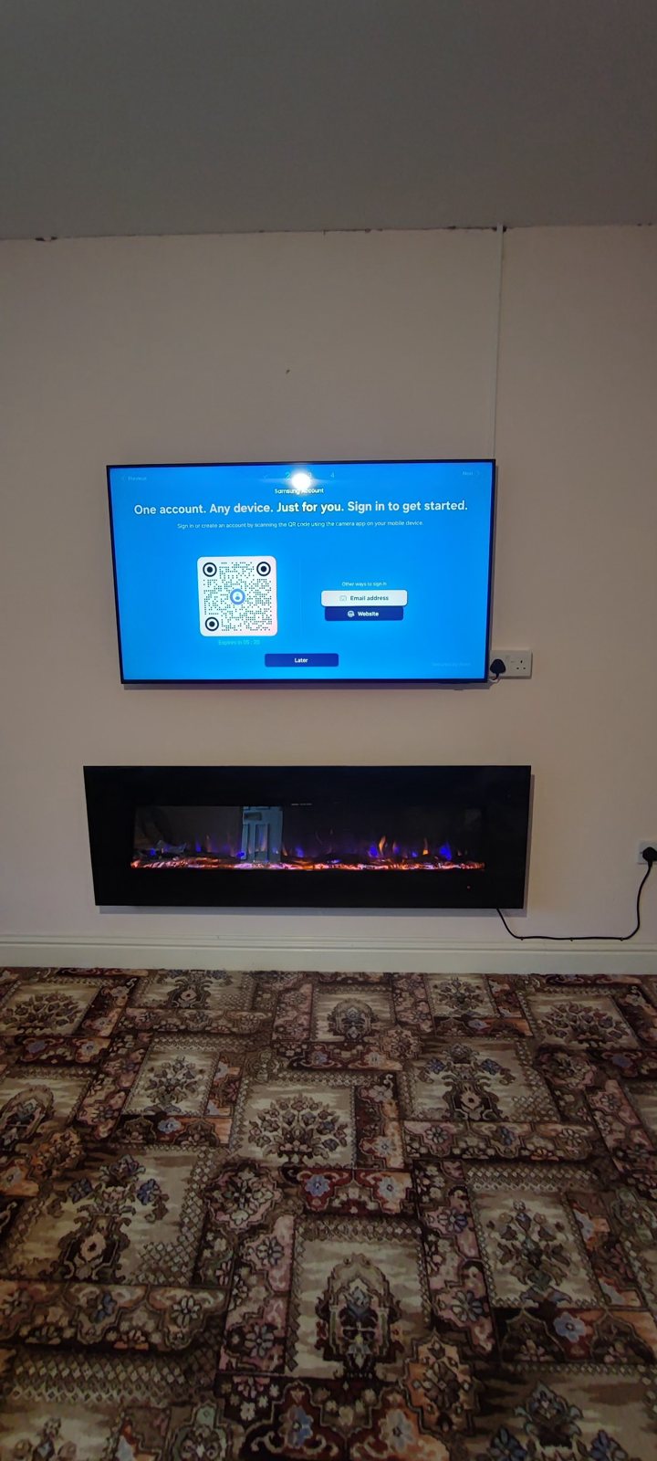 A wall-mounted TV above an electric fire in a living room